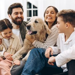 Cheerful family of four, including parents and children, enjoying quality time together while embracing their golden retriever in a cozy home setting