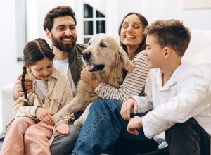Cheerful family of four, including parents and children, enjoying quality time together while embracing their golden retriever in a cozy home setting