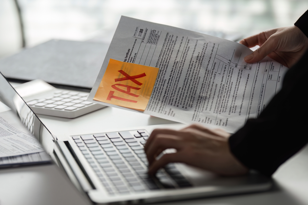 A person handles tax forms while using a laptop, highlighting the critical task of preparing for tax season.