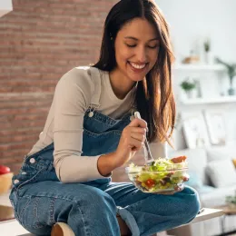 smiling woman sitting on kitchen counter eating a salad