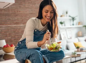 smiling woman sitting on kitchen counter eating a salad