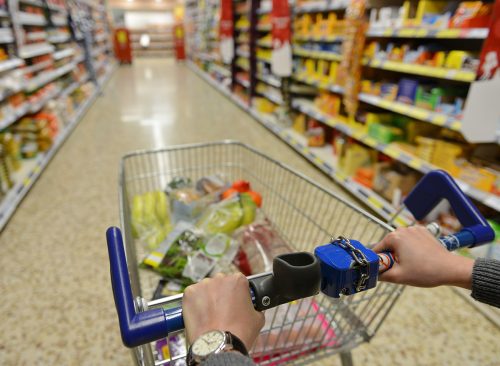 Shopper Pushes a Cart with Grocery Products in Supermarket Aisle - Image Has a Shallow Depth of Field