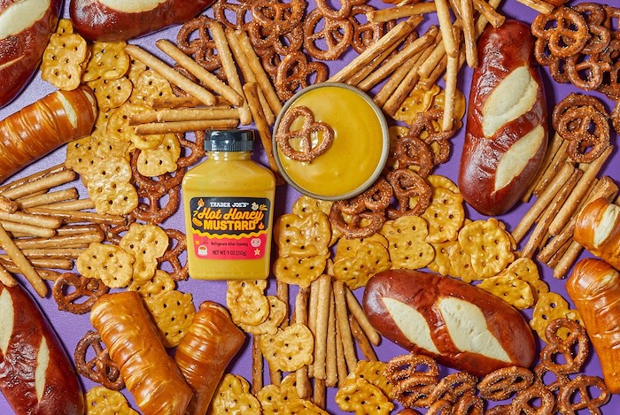 Trader Joe's Hot Honey Mustard shown in a small dish surrounded by different pretzel shapes on a purple surface