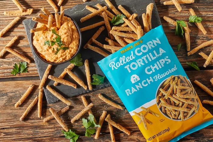 Trader Joe's Ranch Flavored Rolled Corn Tortilla Chips shown on distressed wood surface and slate board, with a dish of Buffalo Chicken Dip and some chips in the dip