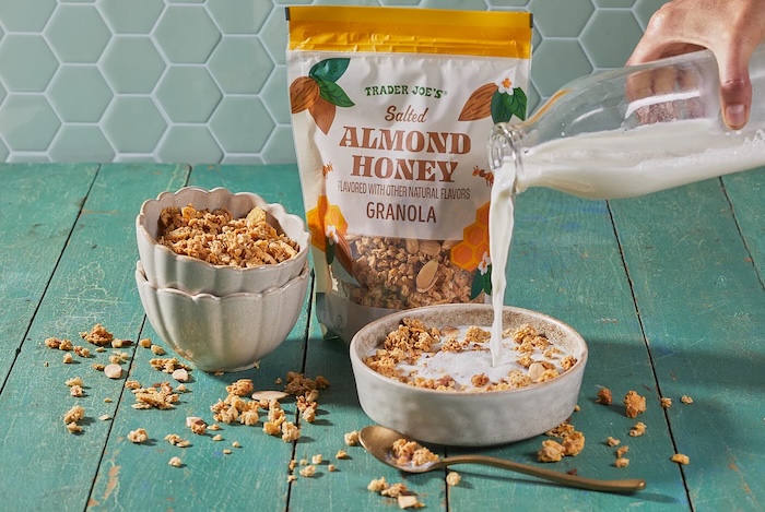 Trader Joe's Salted Almond Honey Granola; bowls shown on green surface, front bowl with milk pour into granola