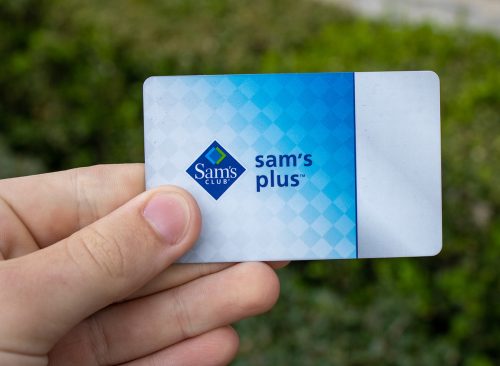 A hand holds a Sam's Club Plus Member membership card, which gives users access to Sam's Club warehouse shopping, rewards, cheap food courts, and chicken