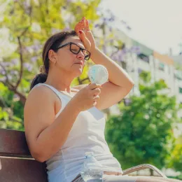 Woman suffering from heat stroke and headache. Holding an electric mini fan sitting outdoors