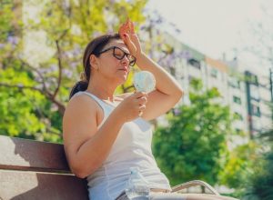 Woman suffering from heat stroke and headache. Holding an electric mini fan sitting outdoors