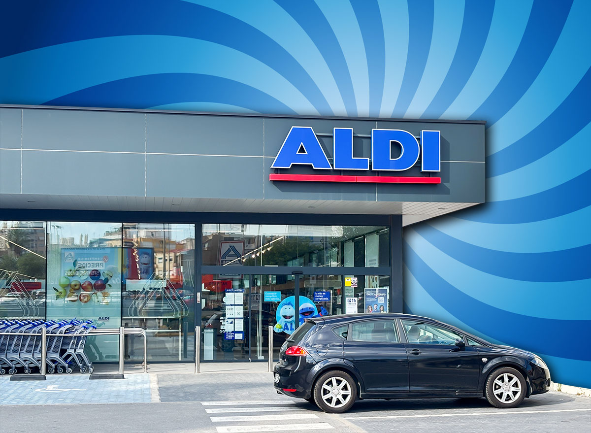 9 Best New Aldi Finds Hitting Shelves in August. Alicante, Spain - May 27, 2025: ALDI store front displays modern design with a parked black vehicle and shopping carts, creating a lively shopping atmosphere