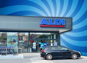 9 Best New Aldi Finds Hitting Shelves in August. Alicante, Spain - May 27, 2025: ALDI store front displays modern design with a parked black vehicle and shopping carts, creating a lively shopping atmosphere