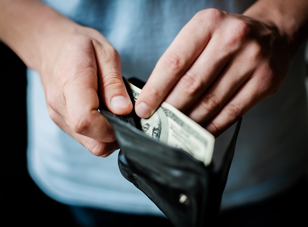 man's hands pulling one hundred dollar bill out of wallet